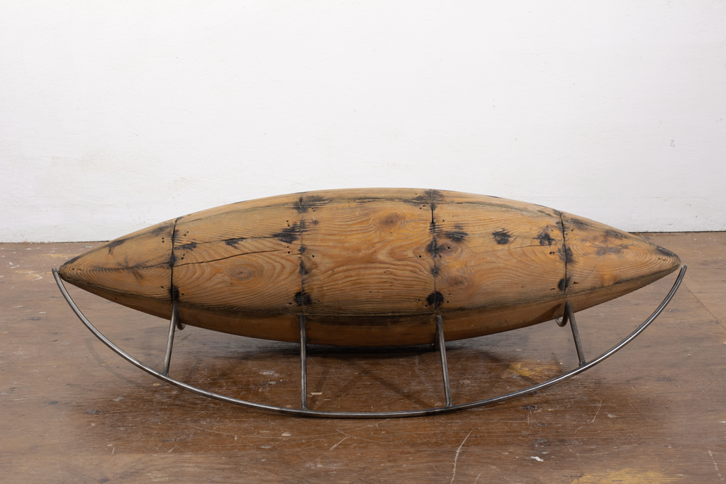 Sculpture de bois ayant vaguement la forme d'un fuselage. Elle porte un réseau de brûlures, montrant qu'elle a servi de matrice dans un travail de chaudronnerie. Elle s'accompagne d'un ouvrage linéaire d'acier inoxydable.