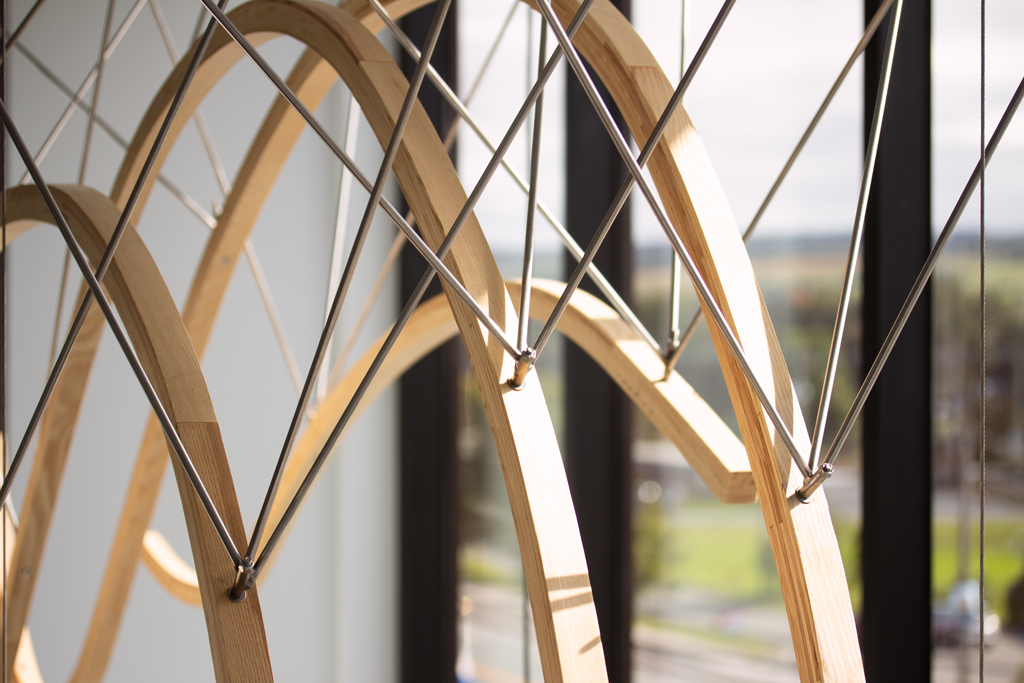 Détail de l'œuvre suspendue Espace géographique de François Mathieu, à la MRC de Nouvelle-Beauce. Elle est faite de bois cintré, de bronze et d'acier inoxydable.