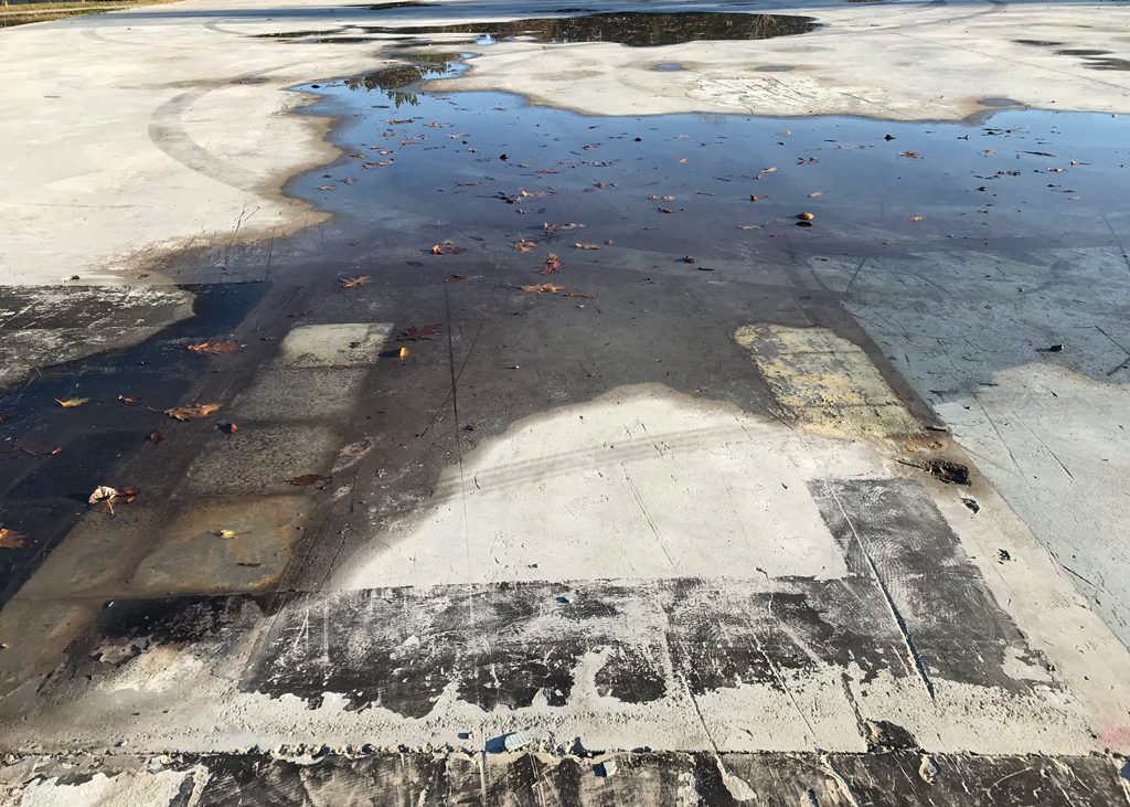 Dalle subsistant après la démolition du centre administratif de Nouvelle-Beauce à Ste-Marie. Par le biais des couvre-planchers arrachés, y voit les traces de l'ancienne organisation spatiale des lieux, encore détrempée après un orage. Situé à quelques mètres de la rivière Chaudière, le bâtiment a été rasé pour cause d'inondation.