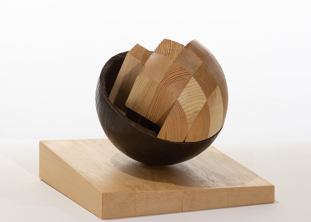 Sculpture sphérique composée partiellement de bois sculpté et de bronze. Elle et posée sur un petit socle de plan incliné, afin de désaxer son centre de gravité.