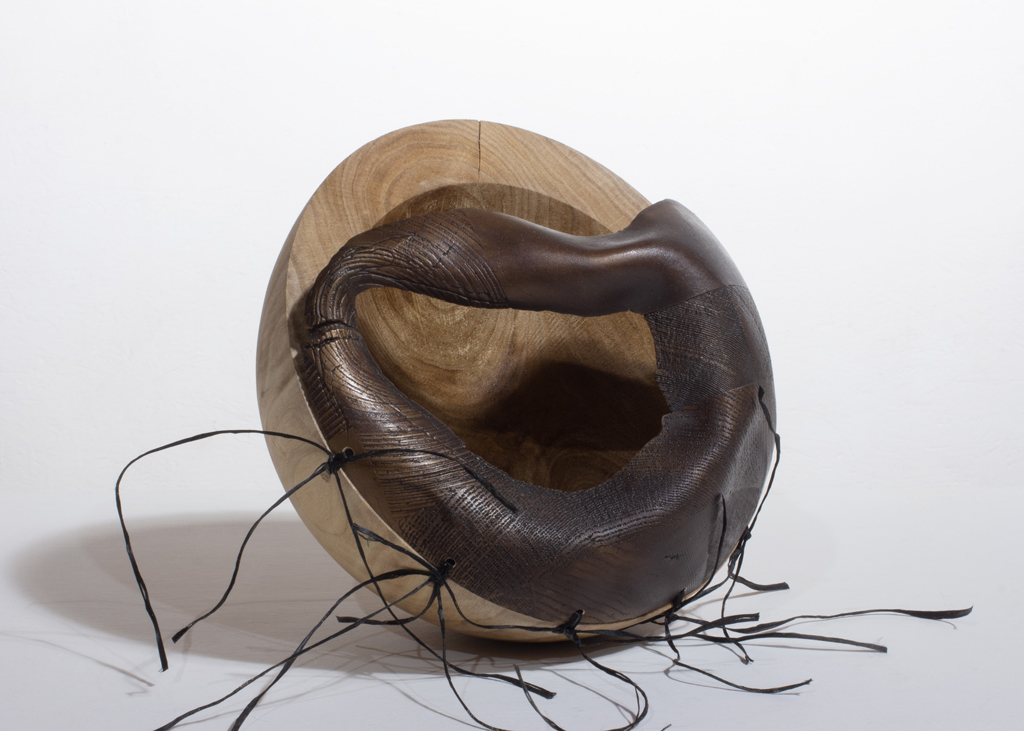 Petite sculpture ronde composée de deux parties. L'une est faite en bronze et cousue sur une moitié en bois sculpté.