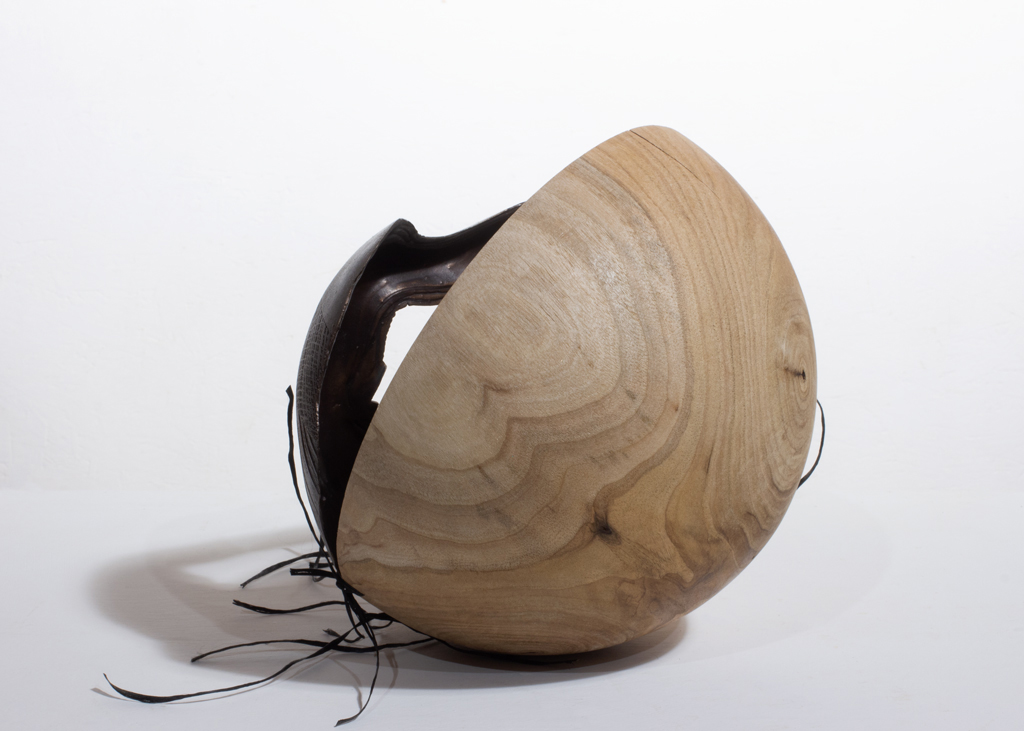 Petite sculpture ronde composée de deux parties. L'une est faite en bronze et cousue sur une moitié en bois sculpté.