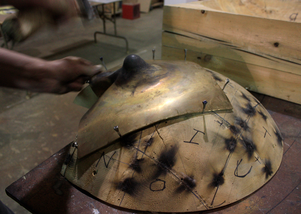 Sculpture de laiton chaudronné en cours de réalisation. On y voit l'une des composantes fortement distorsionnée puis positionnée sur une matrice de bois.
