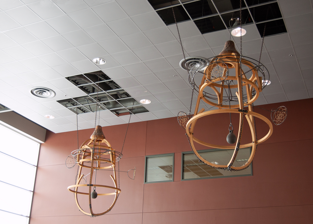 Détail d'une installation sculpturale suspendue. Il s'agit de deux grandes formes de bois fsisant penser à des bouées flottant au-dessus d'une mer de monde.