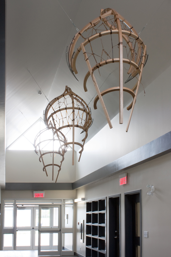 Installation suspendue au sommet d'un étroit corridor. Cette installation comporte trois sculptures ajourées de bois, tressées de babiche, ayant la forme ambiguë d'une embarcation ou d'une feuille d'arbre.