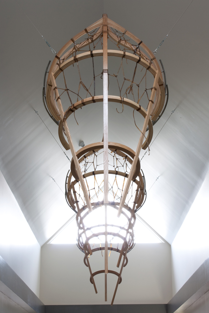 Installation suspendue au sommet d'un étroit corridor. Cette installation comporte trois sculptures ajourées de bois, tressées de babiche, ayant la forme ambiguë d'une embarcation ou d'une feuille d'arbre.