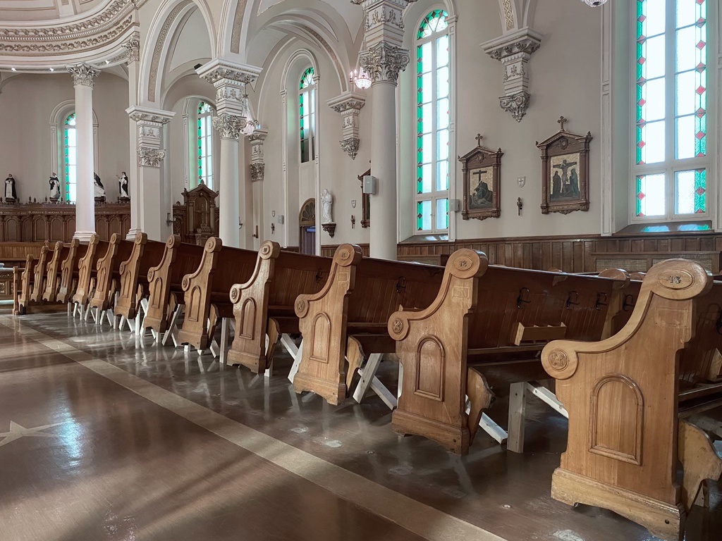 Détail d'une installation sculpturale dans une église. Les bancs sont soulevés à l'aide de bois d'œuvre pour former une grande vague.