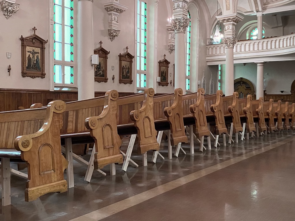 Détail d'une installation sculpturale dans une église. Les bancs sont soulevés à l'aide de bois d'œuvre pour former une grande vague.