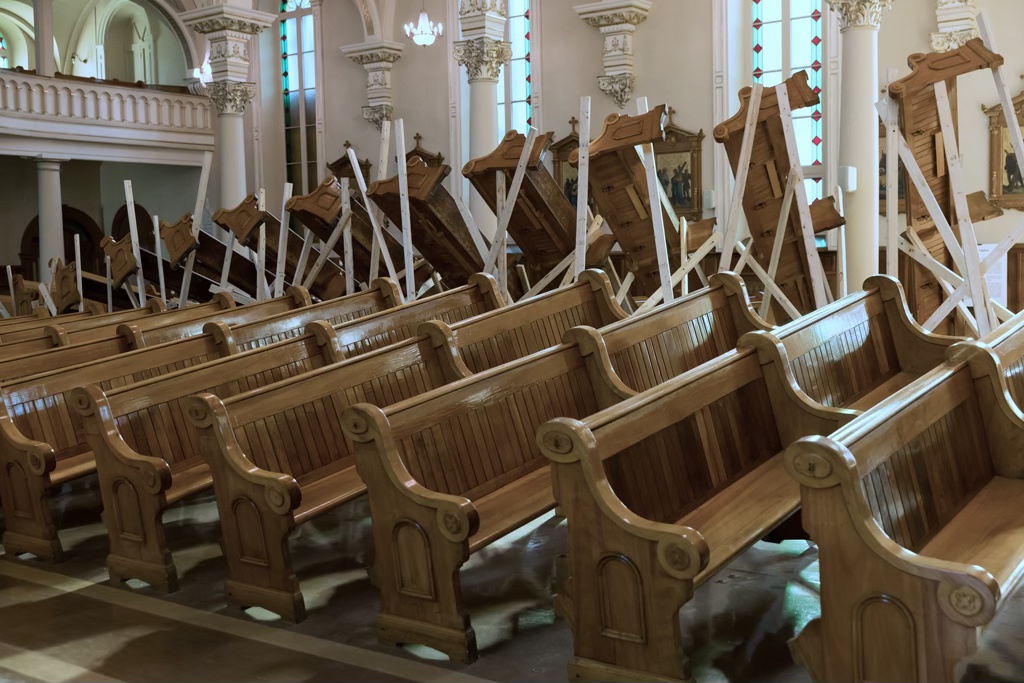 Détail d'une installation sculpturale dans une église. Les bancs sont soulevés à l'aide de bois d'œuvre pour former une grande vague.