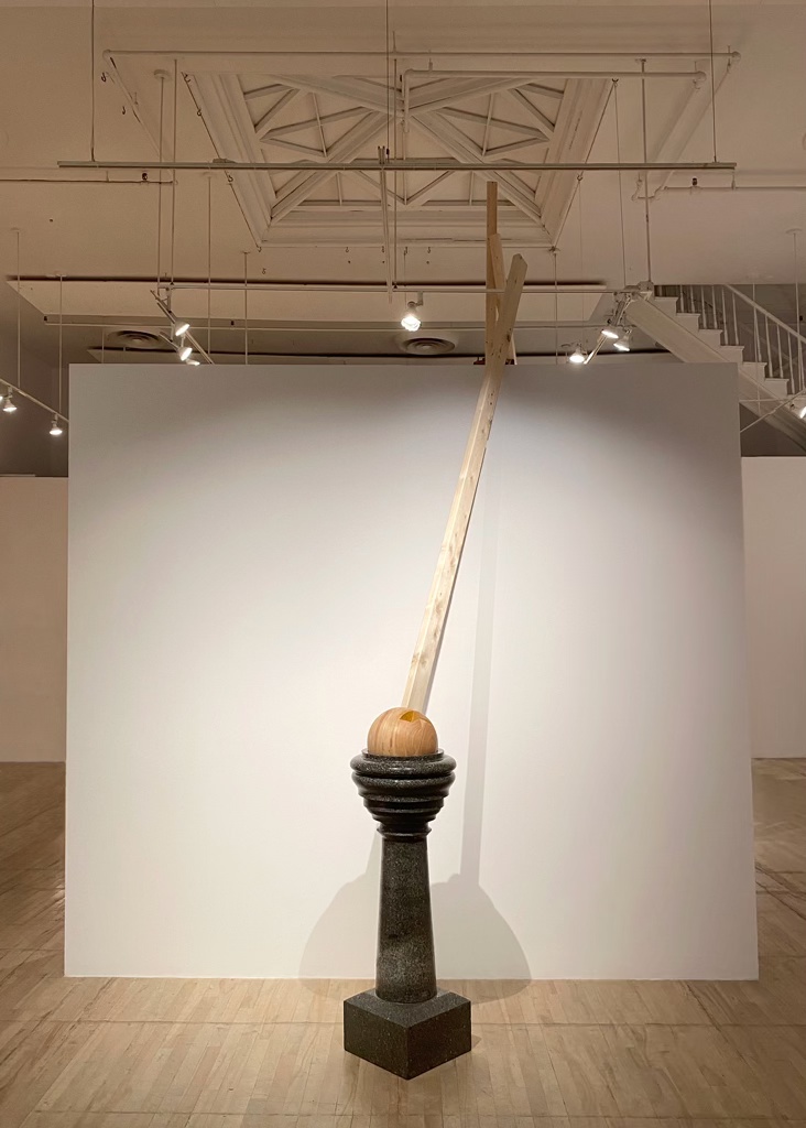 Sculpture faite d'une sphère de bois prolongée d'un 2x4 d'épinette, ajustée dans le creux d'un bénitier de granite comme une pièce mobile.