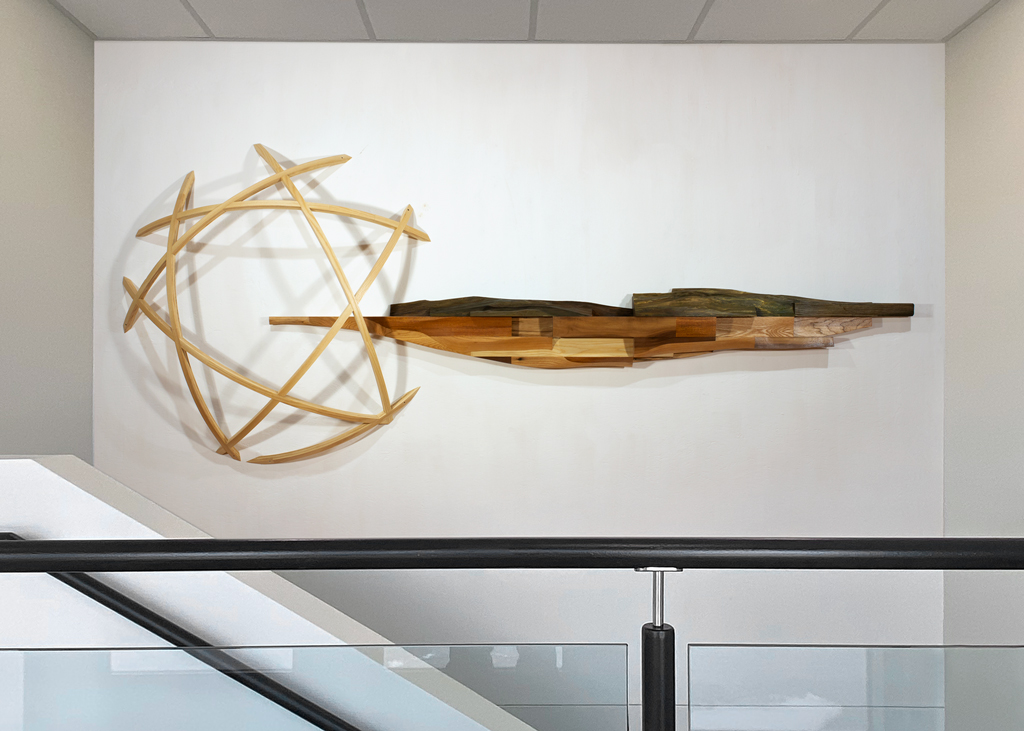 Vue globale de la murale. La section de gauche est un dôme ajouré fait de frêne cintré. À droite, une section longitudinale faite de bois d'essences variées dans la partie inférieure, surmontée d'un horizon fait de bronze.